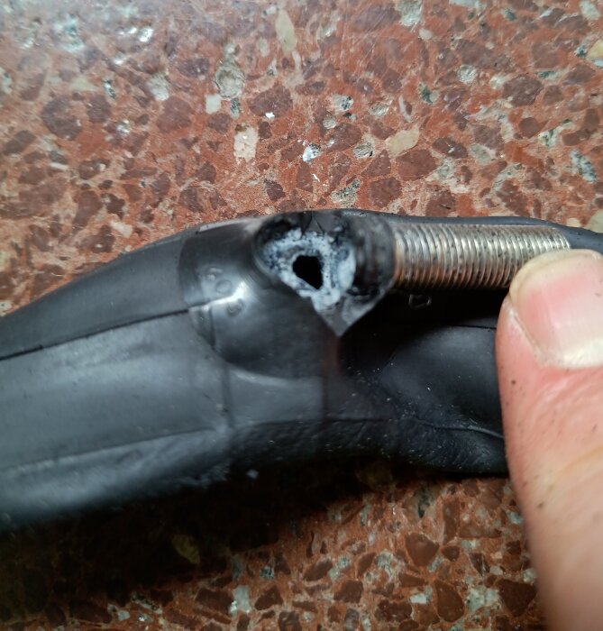 Trasig cykelslang med spricka och ventilstam, nära syning visar skadan; illustrerar problem med hållbarhet hos moderna slangar.