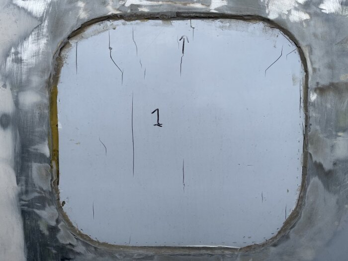 Sprucken skyddsfilm på fönster med märken och repor; omgiven av metallram.