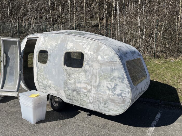 Bilden visar en bastuvagn med öppet dörrparkerat utomhus. Vagnen har flera fönster och en stapel plastlådor står bredvid. Skog i bakgrunden.