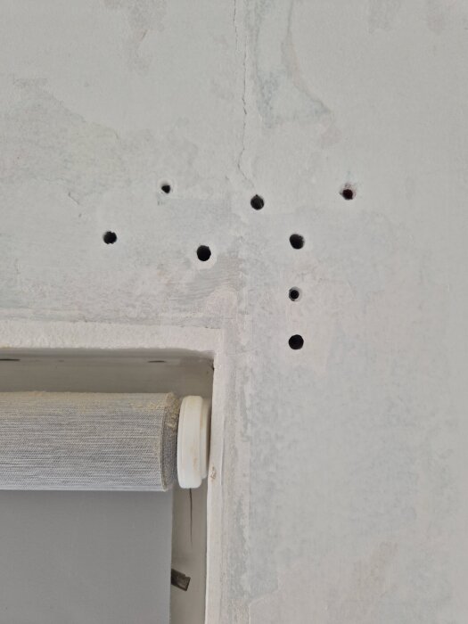 Hål i en lättbetongvägg ovanför ett fönster, troligen för väggmontering; synlig fönsterjalusi i nederkant.