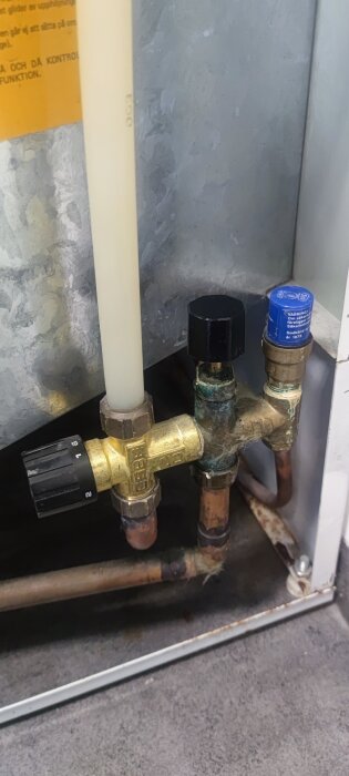 Vattenrör med ventiler under varmvattenberedare i tvättstuga, en svart och en blå ventil syns tydligt.