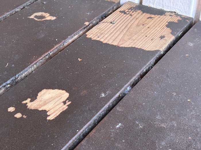 Altanbrädor med avflagnad mörk färg, ytan visar trä under, tecken på slitage och behov av underhållsarbete som slipning och ommålning.