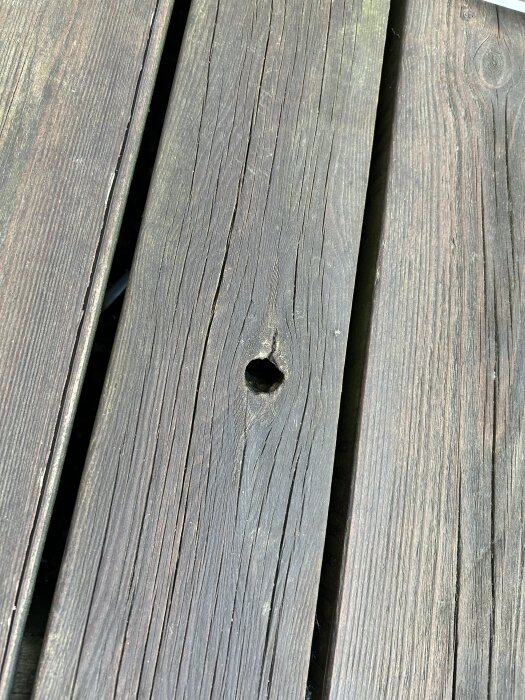 Slitet trädäck med synlig hål och flagnande yta.