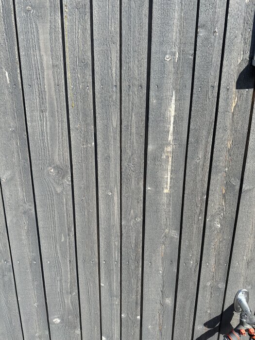 Grånad träfasad med ljusare fläckar och slitage, potentiellt orsakade av bristande lasyrskydd.