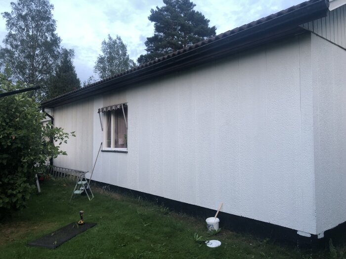 Husfasad nymålat vitt, med trästegar bredvid och målburk på marken.