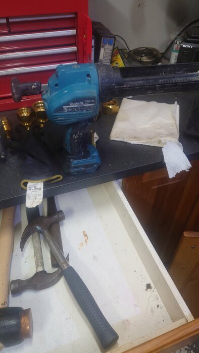 Blå Makita caulking gun placerad på arbetsbänk, omgiven av handverktyg och tillbehör i ett garage eller verkstad.