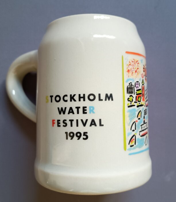 Mugg med texten "Stockholm Water Festival 1995" och färgglad illustration av en stad och fyrverkerier.