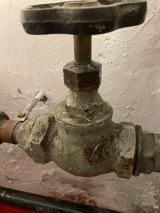 Gammal rostig vattenkran från 1942 med tecken på slitage och korrosion mot en sliten vägg i en byggmiljö.