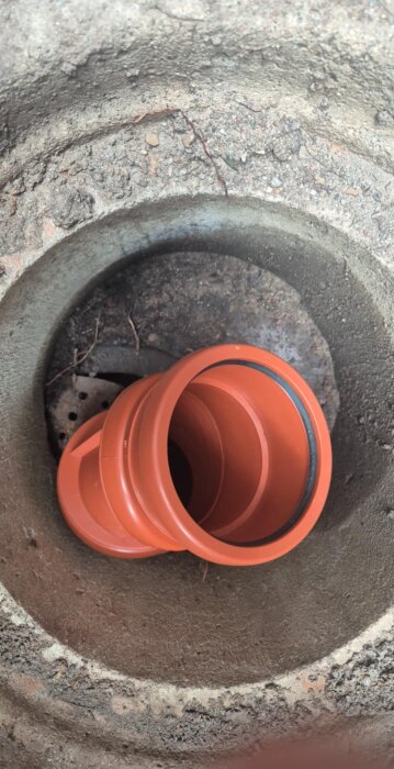 Cementrör med ett orange plaströr inuti och ett gjutjärnslock längst ner i en brunn.