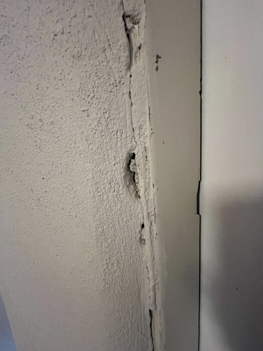Sprukket og skadet pusset vegg ved dørkarm med synlige sprekker og hull, utbedret med puss C men trenger ny justering.