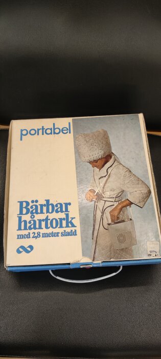 Förpackning av portabel hårtork med bild på person i badrock och huva, text "Bärbar hårtork med 2,8 meter sladd".