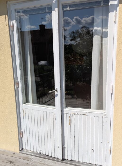 Slitna altandörrar med glaspartier, avskavd vit färg och behov av renovering. Dagsljuset speglas i glaset.
