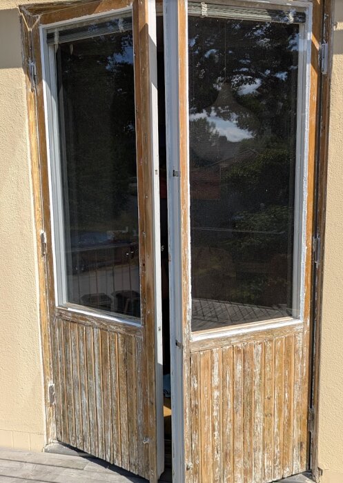 Slitna altandörrar med avskavd färg som öppnar sig mot en solig utsikt, del av renoveringsprojekt med fokus på skrapning och målning.