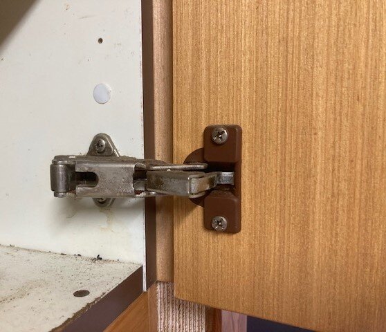 Brunt plastgångjärn fäst på insidan av en skåpslucka i ett gammalt 80-tals-kök.