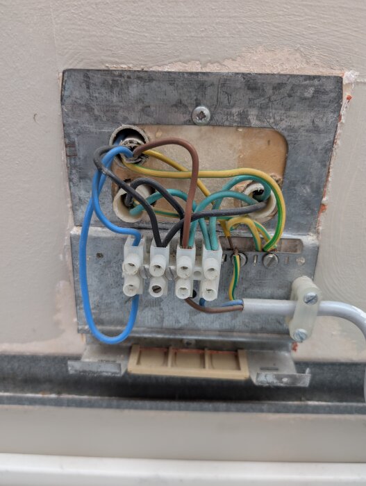 Eluttag med flera kablar, inklusive en blå och brun kabel, anslutna till kopplingspunkter på väggen.