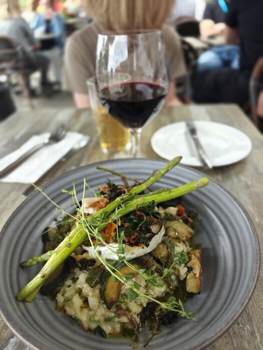 Kantarellrisotto med sparris, dekorerad med örter, serverad med ett glas rött vin på en restaurang.