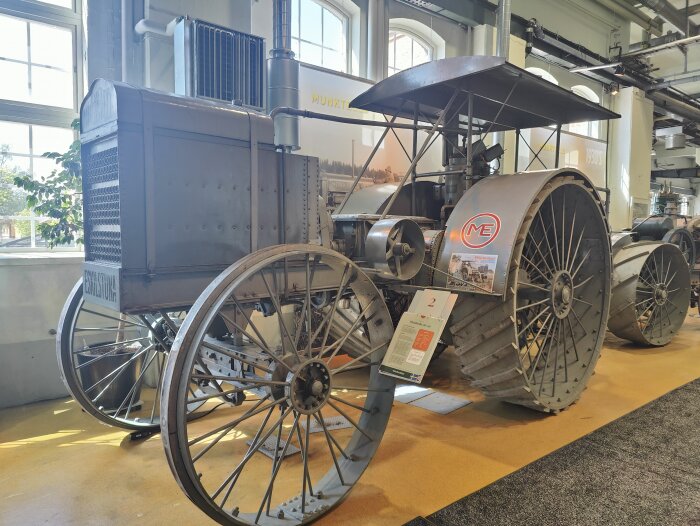 Traktor från Munktellmuseet i Eskilstuna, utställd inomhus med stora hjul och en svart takskärm.