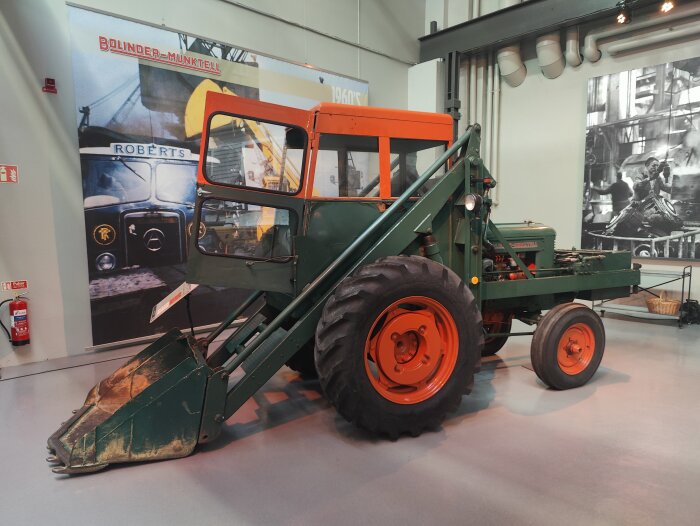 Historisk grön och orange traktor med skopa visas på Munktellmuseet i Eskilstuna.