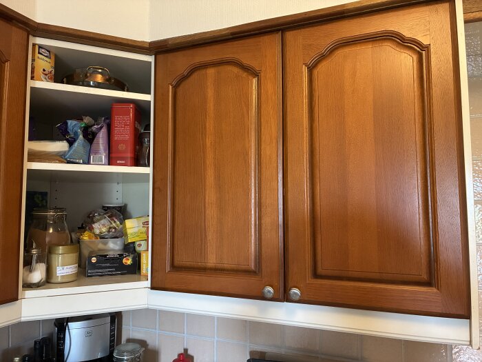 Köksluckor i trä med klassisk design och rundade hörn, öppet hörnskåp med kryddor och matvaror.