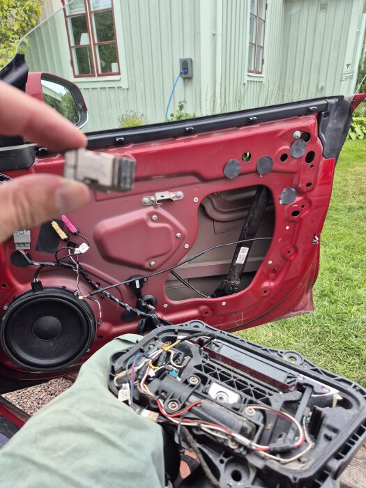 Rött bildörrspanel syns med inre mekanismer exponerade; en hand håller en liten metallbit framför dörren.