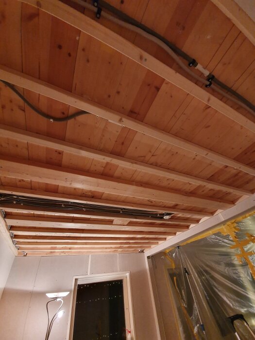 Reglat tak med träpanel och synliga elrör i en byggarbetsplats.