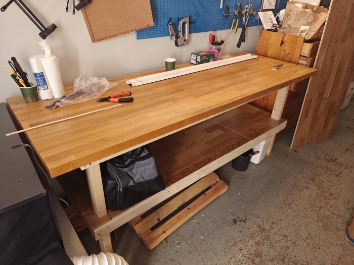 Arbetsbänk av trä med verktyg och förvaringshylla gjord av klickgolv i ett organiserat garage.