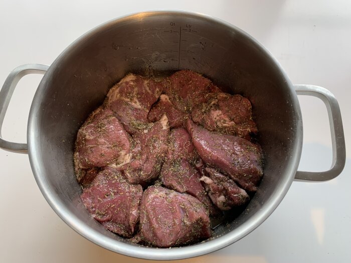 Marinerad lammkött läggs i en stor metallgryta, redo för grillning.