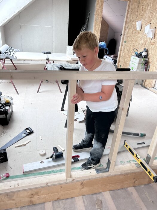 Barn som bygger en trästomme för en vägg i ett renoveringsprojekt. Verktyg och byggmaterial syns omkring.