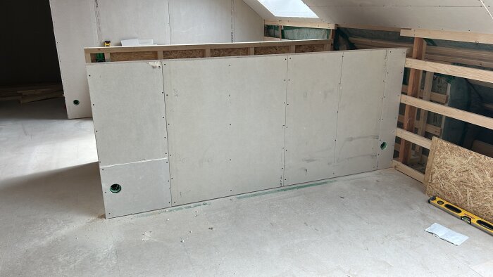 Gipsade väggar under konstruktion på en byggarbetsplats med OSB-skydd i bakgrunden och verktyg på golvet.