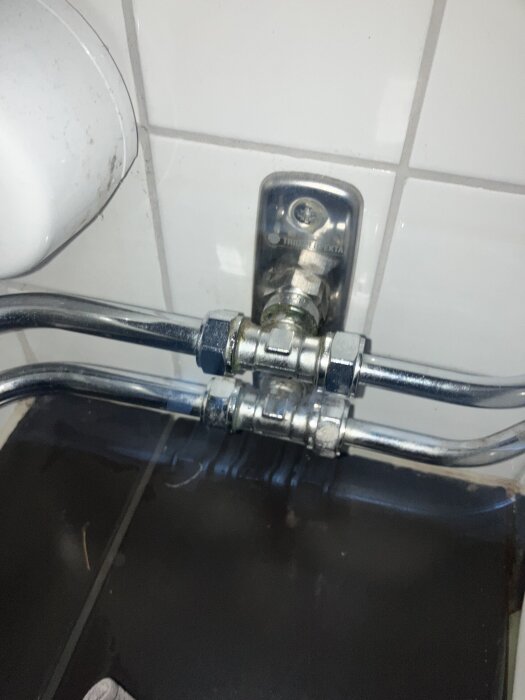 Metallrör och koppling på en vägg i ett badrum, potentiellt orsakar vattenläckage när vatten används i köket.