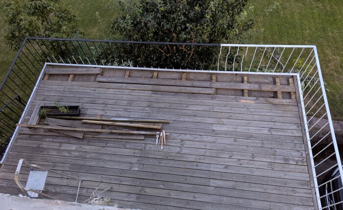 Nylagd altan med delvis ofärdig ram och räcke, träbrädor och några verktyg ligger spridda, gräsmatta och träd syns i bakgrunden.