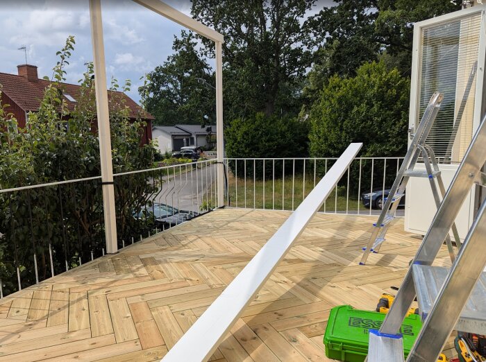 Nybyggd altan med trägolv och del av takstomme. Stegar och verktyg syns, omgivning med bostadshus och träd i bakgrunden.