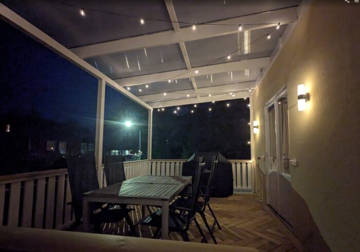 Upplyst altan med tak, sittgrupp och ljusslingor, tagen på kvällen.