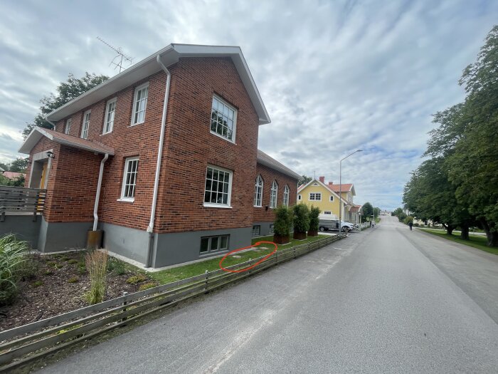 Tegelhals hus med röda tegelväggar, vita stuprör och grå sockel synligt utmed en väg i ett bostadsområde.