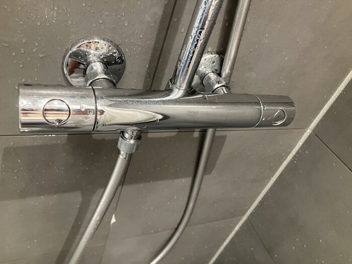 Duschblandare av märket Grohe monterad på en våtrumsvägg, fotograferad med vattenstänk på ytan.