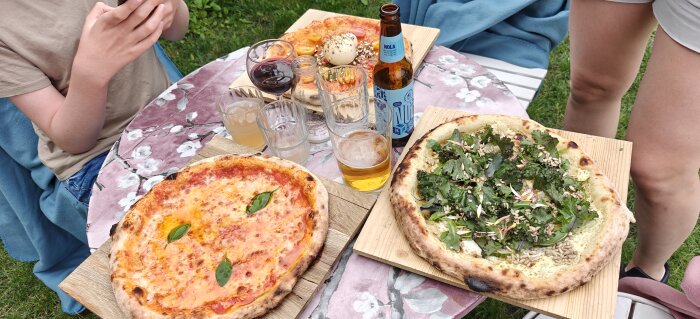 Två pizzor på ett bord utomhus med drycker och personer som deltar i en pizzakväll i Växjö.