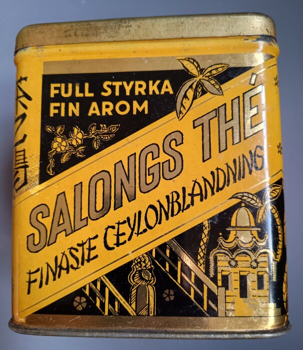 En gul och svart vintage teburk med texten "Full styrka fin arom, Salongs thé, Finaste Ceylonblandning" samt grafiska illustrationer.