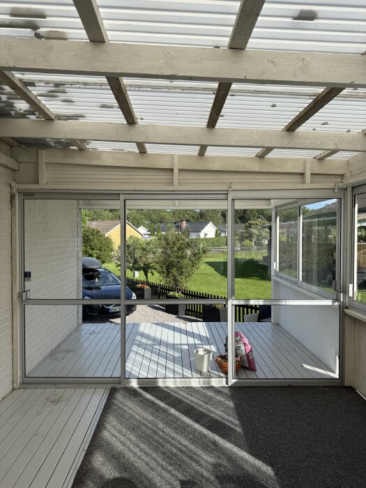 Skjutpartier mot trappan med vita plankgolv, en grå matta, en vit hink och en rosa påse. Trädgård och hus syns utanför.