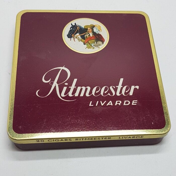 Röd plåtburk för Ritmeester-cigarrer med guldkanter och bild av en man med häst.