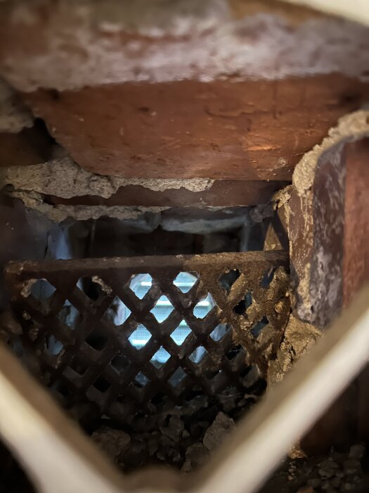 Friskluftsventil i tegelvägg utan rör, visar ett hål med ett metallgaller och synligt ljus genom öppningen.