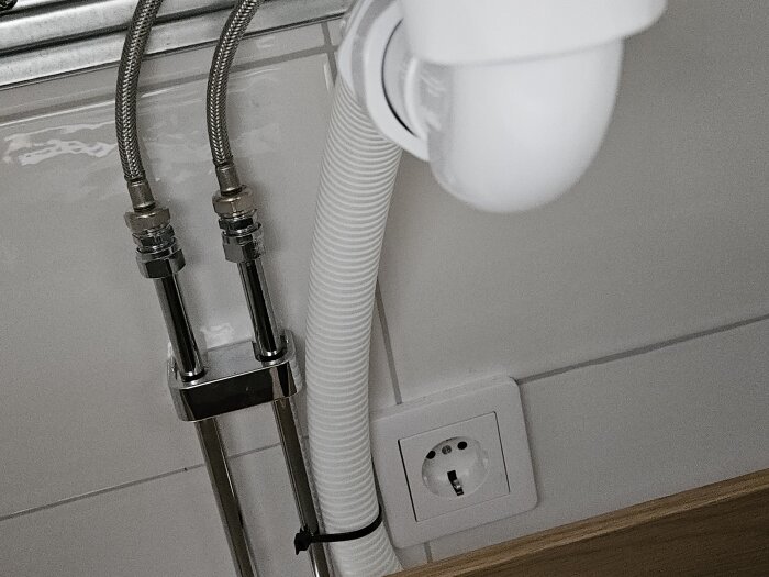 Vattenlås och kopplingsplint under diskbänk med synliga slangar och eluttag.
