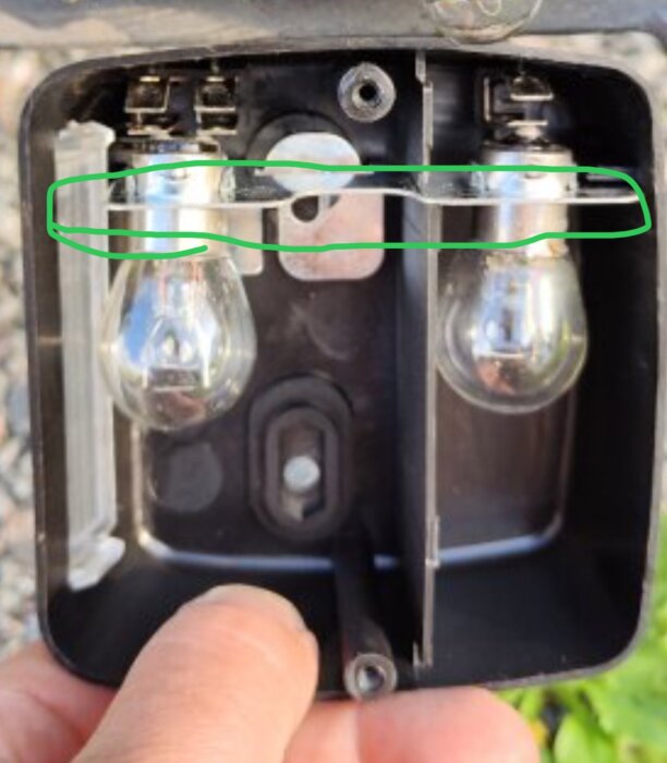 Fokus på två glödlampor i en lampa med ett inringat område för jordanslutning, visar markering av potentiell kabelskoanslutning.