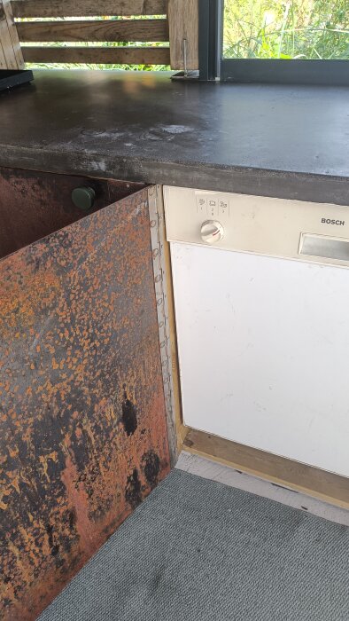 Rostig utdragslåda i ett utekök med en vit Bosch diskmaskin i bakgrunden.