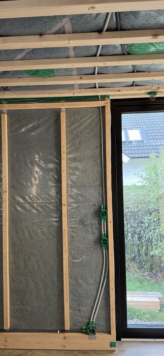 Stående träreglar 45x45 mm med installationsskikt, isolering och eldragning mot en vägg med glasad dörr bredvid.