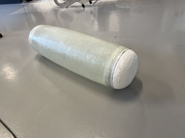 Cylinderformad struktur av cellplast, täckt med epoxi, liggande på ett golv. Skapad för ett bastuprojekt, avsedd att rymma batteri och elcentral.