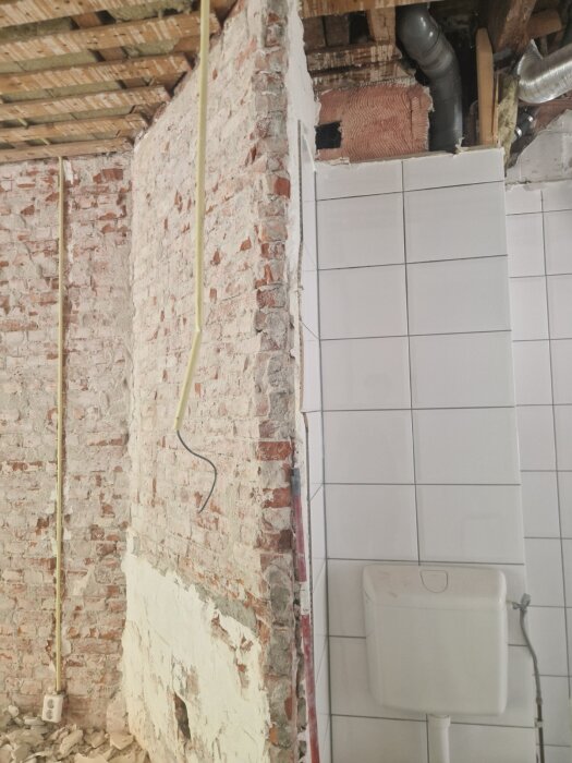 Gammal skorsten i tegel, delvis riven med synliga rör i taket och kaklad vägg med en toalettcistern.