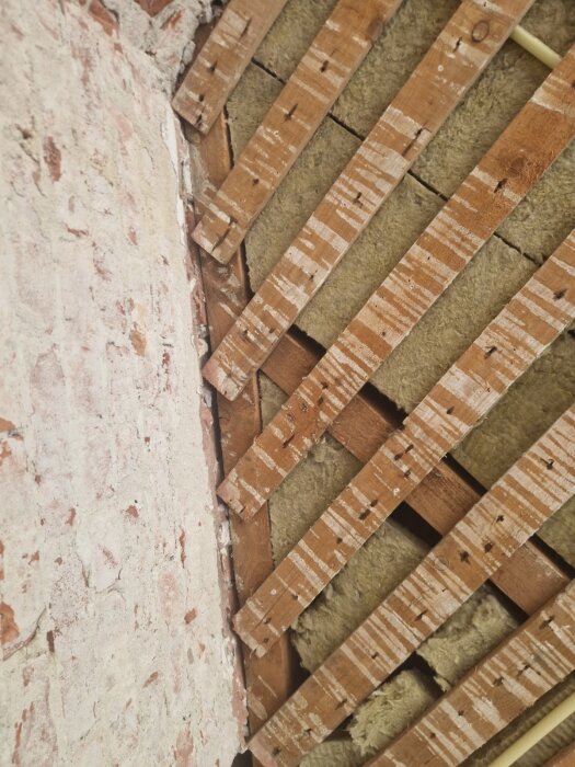 Gammal skorsten med delvis borttaget tegel, synliga takreglar och isolering i ett renoveringsprojekt.