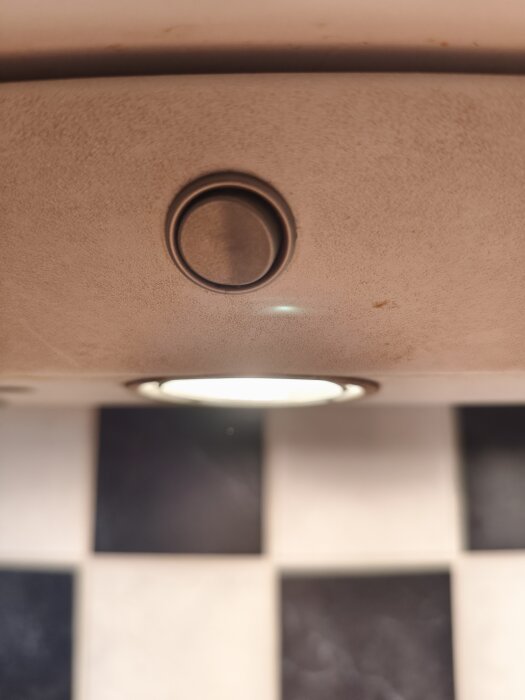 Knapp och belysning på ljusramp över en köksbänk med svartvita kakelplattor i bakgrunden.