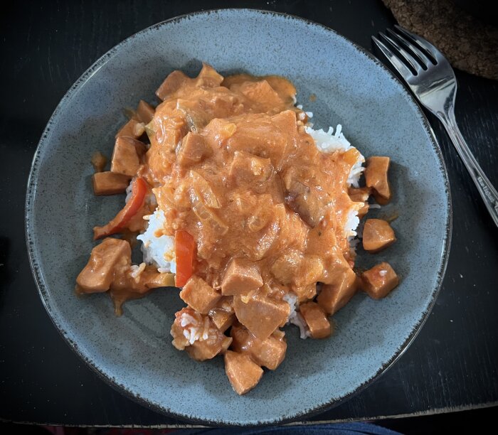 Tallrik med korvgryta innehållande falukorv, lök, champinjoner, squash och paprika, serverad över ris.