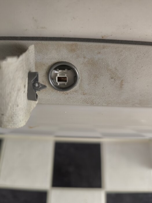 Närbild av en ljusramp utan modellbeteckning, med saknad knapp vid sidan om ett runt uttag, omgiven av en rutmönstrad bakgrund.